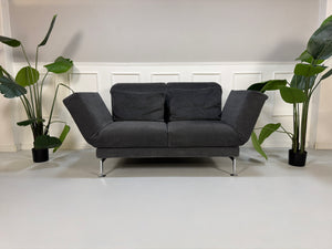 Gebrauchtes graues Stoffsofa Brühl Modell Moule Small vor einer modernen Wand