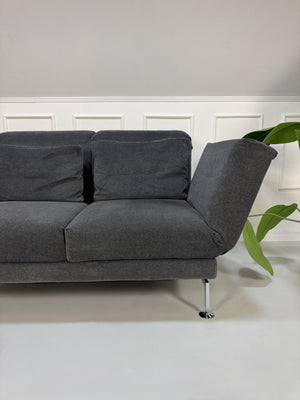 Gebrauchtes graues Stoffsofa Brühl Modell Moule Small vor einer modernen Wand