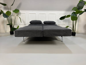 Gebrauchtes graues Stoffsofa Brühl Modell Moule Small vor einer modernen Wand