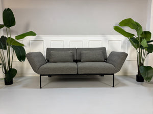 Gebrauchtes graues Stoffsofa Brühl Modell Roro Soft vor einer modernen Wand.