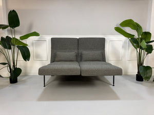 Gebrauchtes graues Stoffsofa Brühl Modell Roro Soft vor einer modernen Wand.