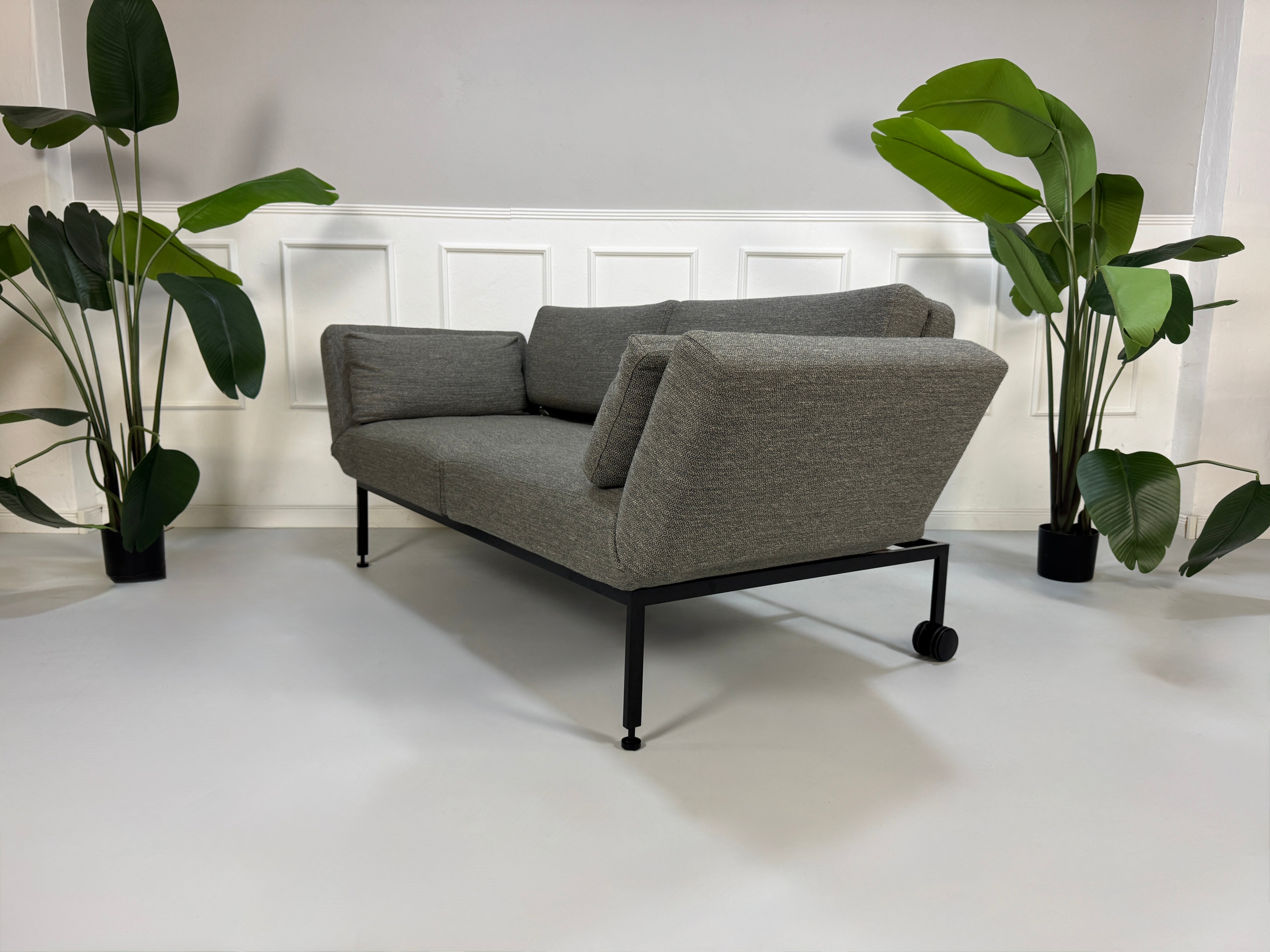 Gebrauchtes graues Stoffsofa Brühl Modell Roro Soft vor einer modernen Wand.