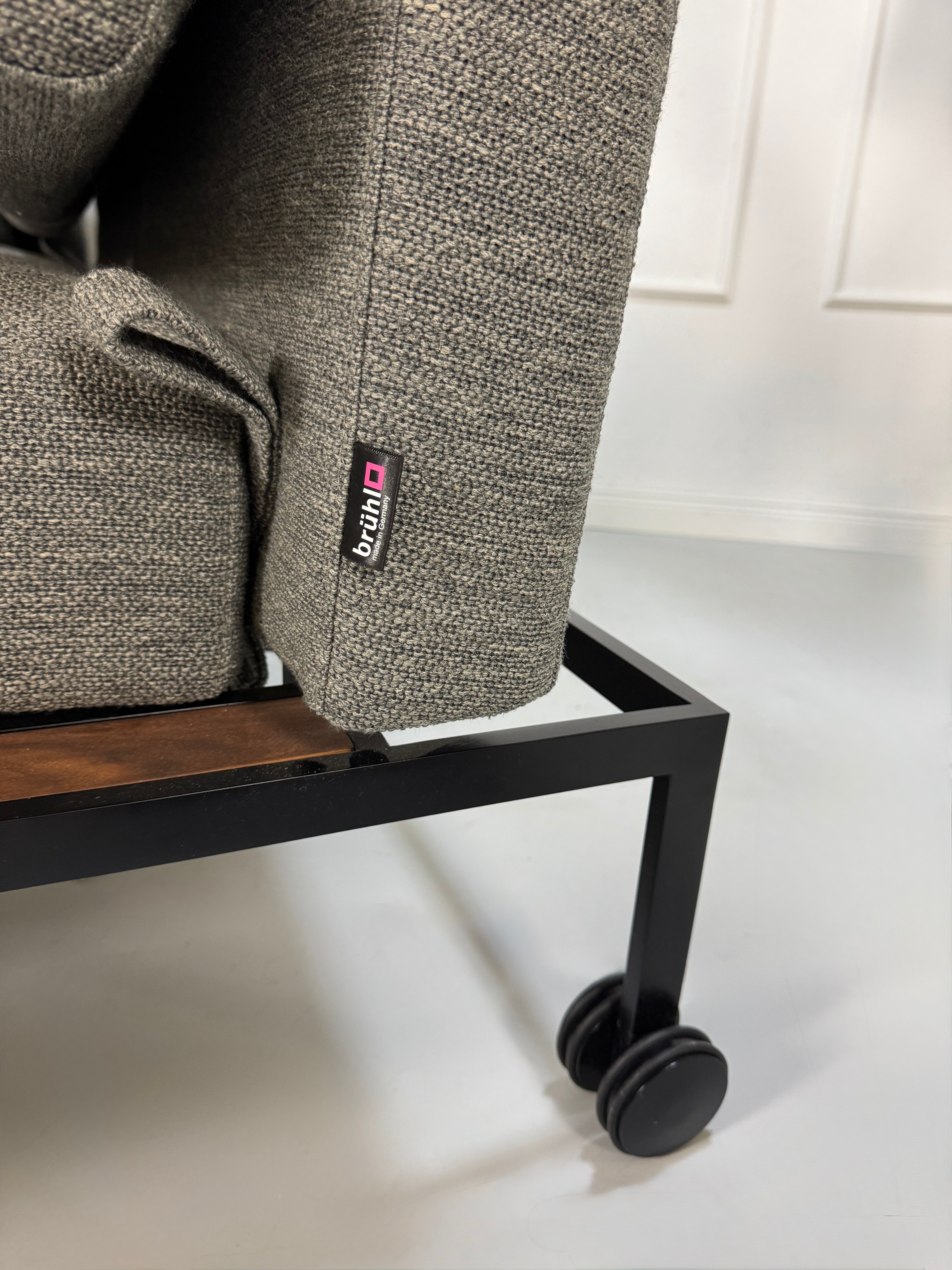 Gebrauchtes graues Stoffsofa Brühl Modell Roro Soft vor einer modernen Wand.