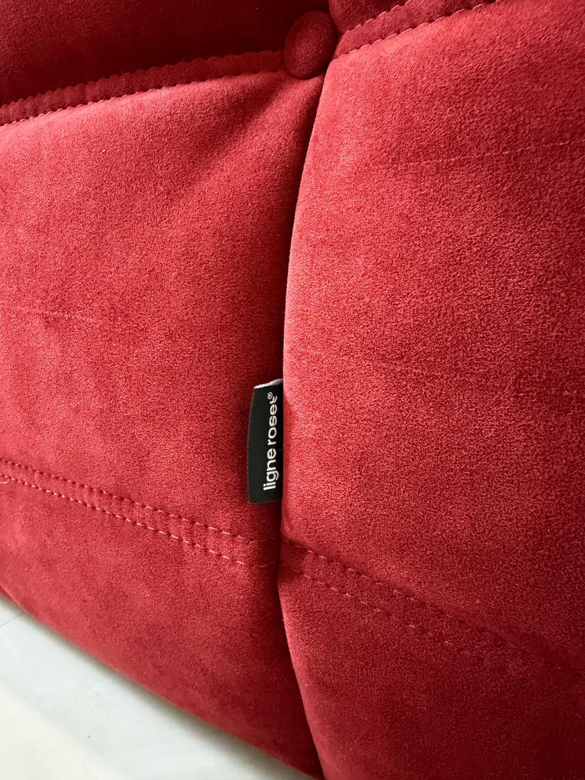 Gebrauchtes rotes Stoffsofa Ligne Roset Modell Togo vor einer modernen Wand.