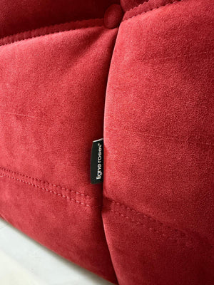 Gebrauchtes rotes Stoffsofa Ligne Roset Modell Togo vor einer modernen Wand.