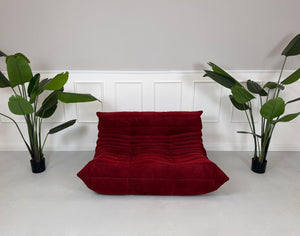 Gebrauchtes rotes Stoffsofa Ligne Roset Modell Togo vor einer modernen Wand.