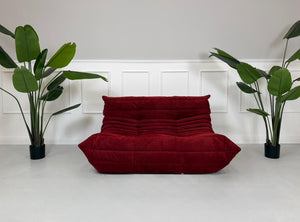 Gebrauchtes rotes Stoffsofa Ligne Roset Modell Togo vor einer modernen Wand.