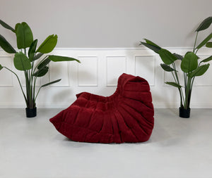 Gebrauchtes rotes Stoffsofa Ligne Roset Modell Togo vor einer modernen Wand.
