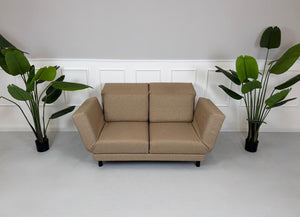Gebrauchtes braunes Stoffsofa Brühl Modell Moule Small vor einer modernen Wand.