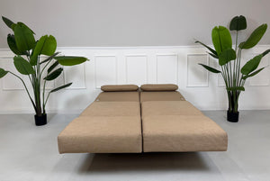 Gebrauchtes braunes Stoffsofa Brühl Modell Moule Small vor einer modernen Wand.