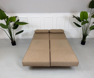 Gebrauchtes braunes Stoffsofa Brühl Modell Moule Small vor einer modernen Wand.
