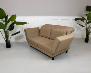Gebrauchtes braunes Stoffsofa Brühl Modell Moule Small vor einer modernen Wand.