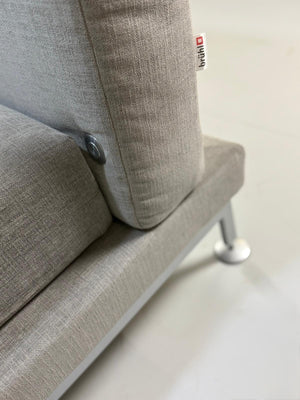 Gebrauchtes graues Stoffsofa Brühl Modell Moule vor einer modernen Wand.