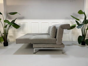 Gebrauchtes graues Stoffsofa Brühl Modell Moule vor einer modernen Wand.