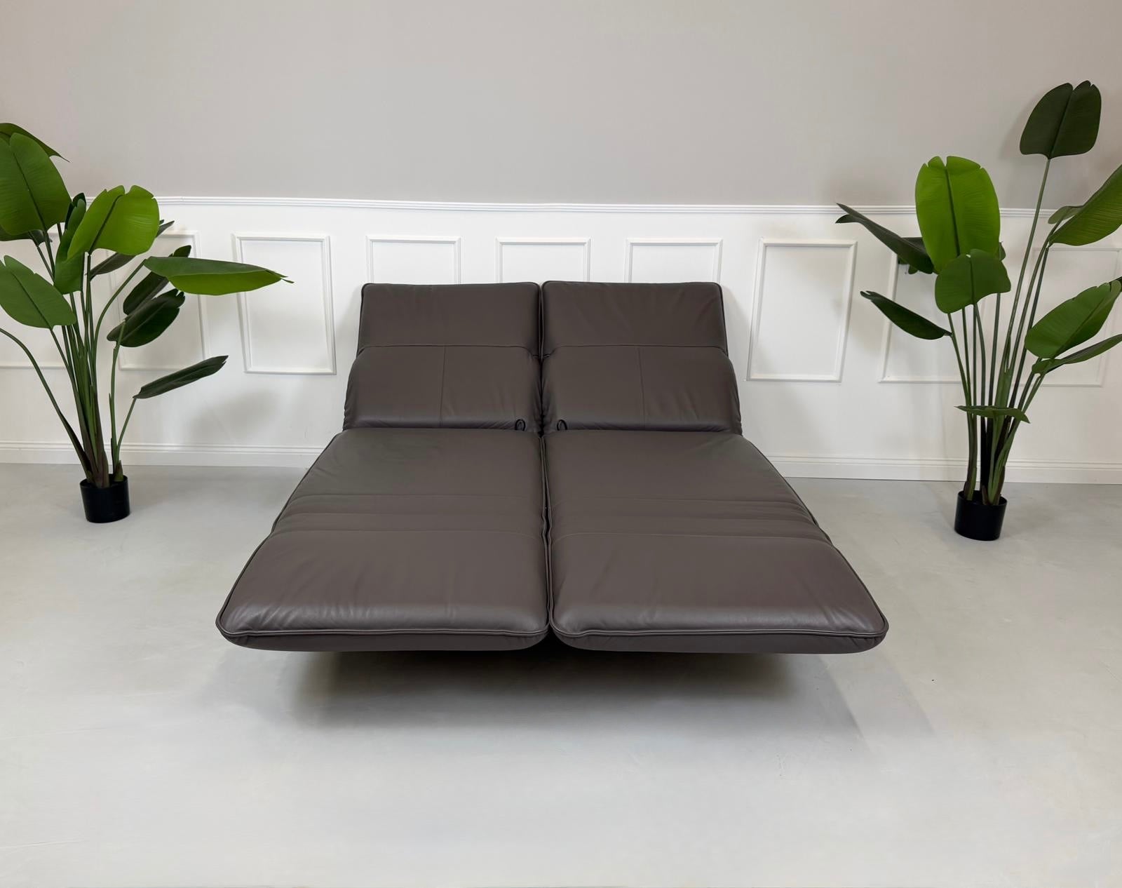 Gebrauchtes braunes Ledersofa Rolf Benz Modell Mera vor einer modernen Wand.