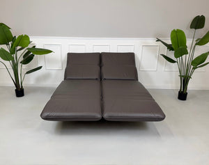 Gebrauchtes braunes Ledersofa Rolf Benz Modell Mera vor einer modernen Wand.