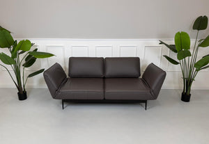 Gebrauchtes braunes Ledersofa Rolf Benz Modell Mera vor einer modernen Wand.