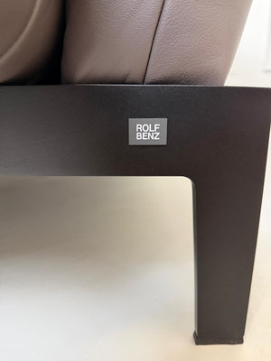 Gebrauchtes braunes Ledersofa Rolf Benz Modell Mera vor einer modernen Wand.