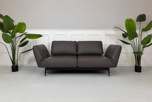 Gebrauchtes braunes Ledersofa Rolf Benz Modell Mera vor einer modernen Wand.