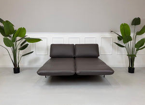 Gebrauchtes braunes Ledersofa Rolf Benz Modell Mera vor einer modernen Wand.