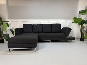 Gebrauchtes graues Stoffsofa Brühl Modell FourTwo vor einer modernen Wand.