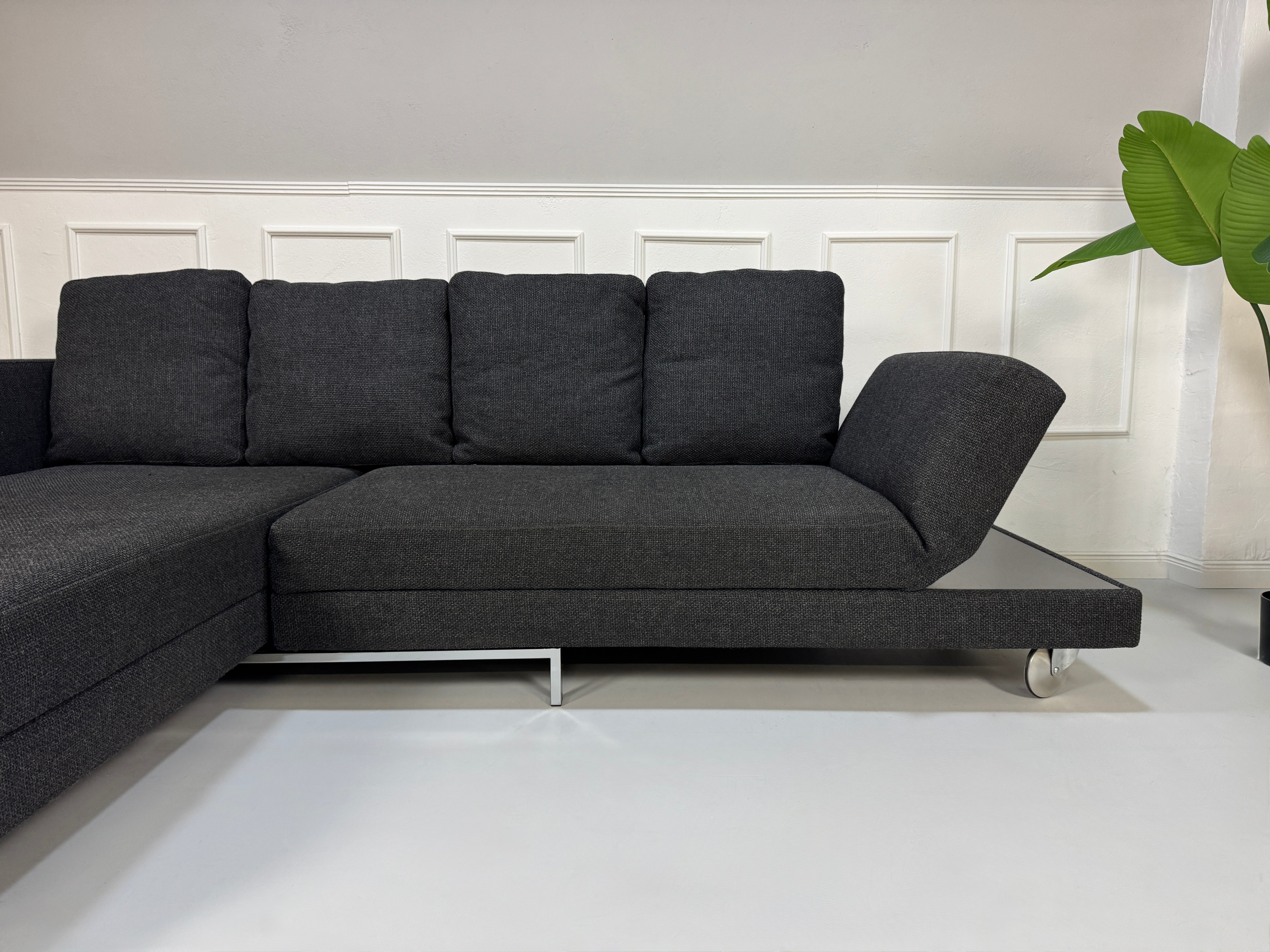 Gebrauchtes graues Stoffsofa Brühl Modell FourTwo vor einer modernen Wand.