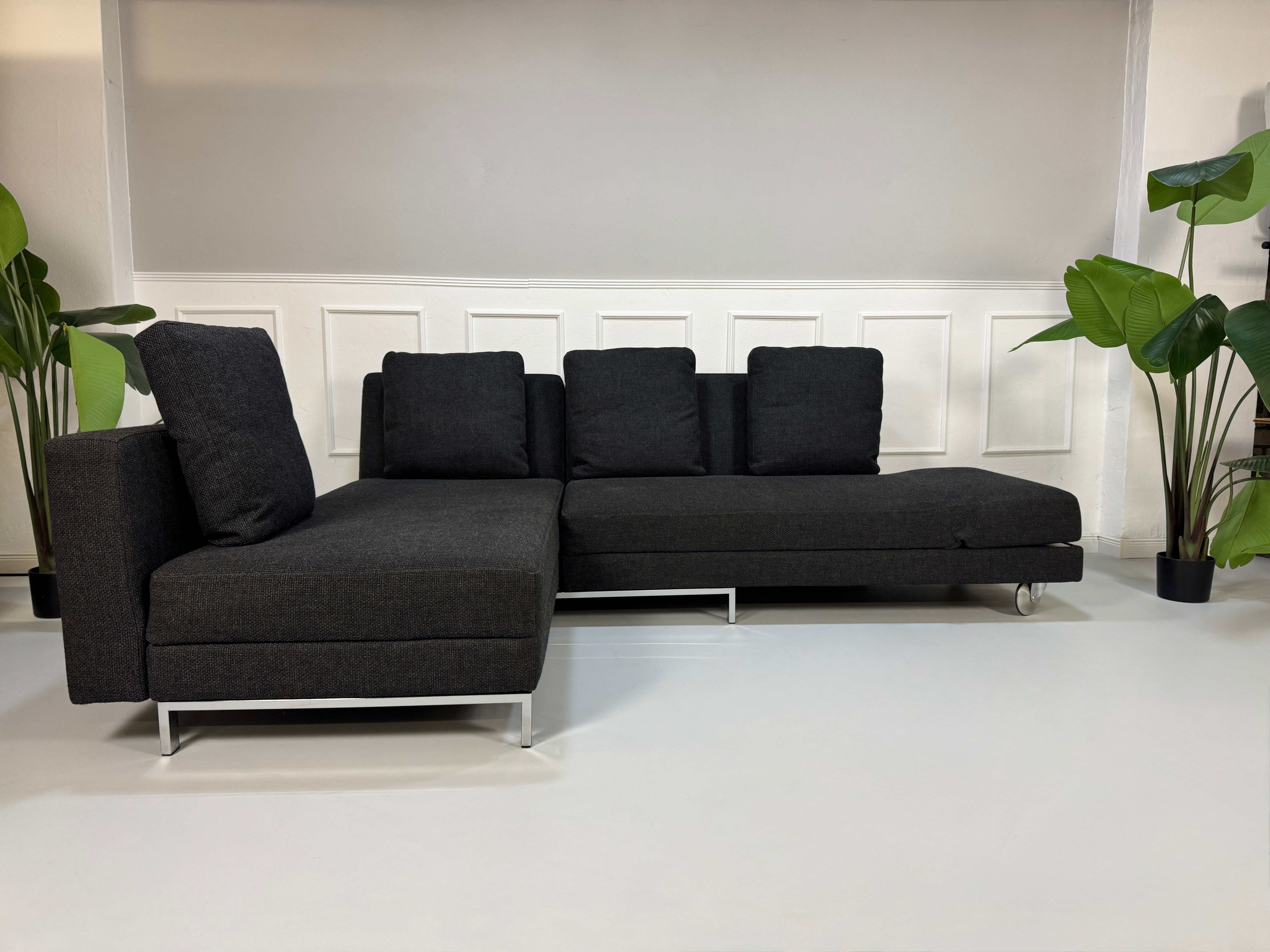 Gebrauchtes graues Stoffsofa Brühl Modell FourTwo vor einer modernen Wand.