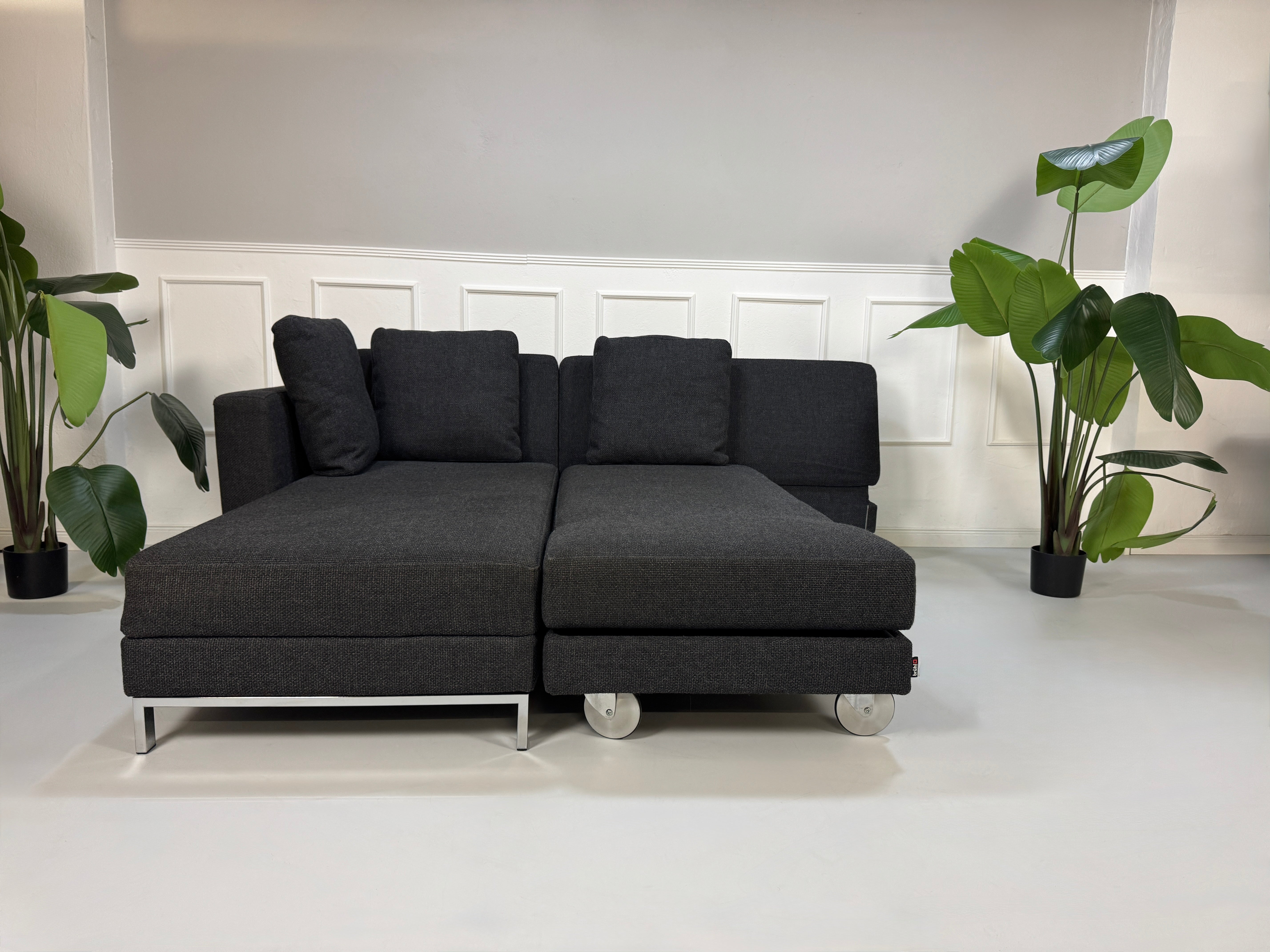 Gebrauchtes graues Stoffsofa Brühl Modell FourTwo vor einer modernen Wand.