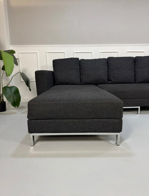 Gebrauchtes graues Stoffsofa Brühl Modell FourTwo vor einer modernen Wand.