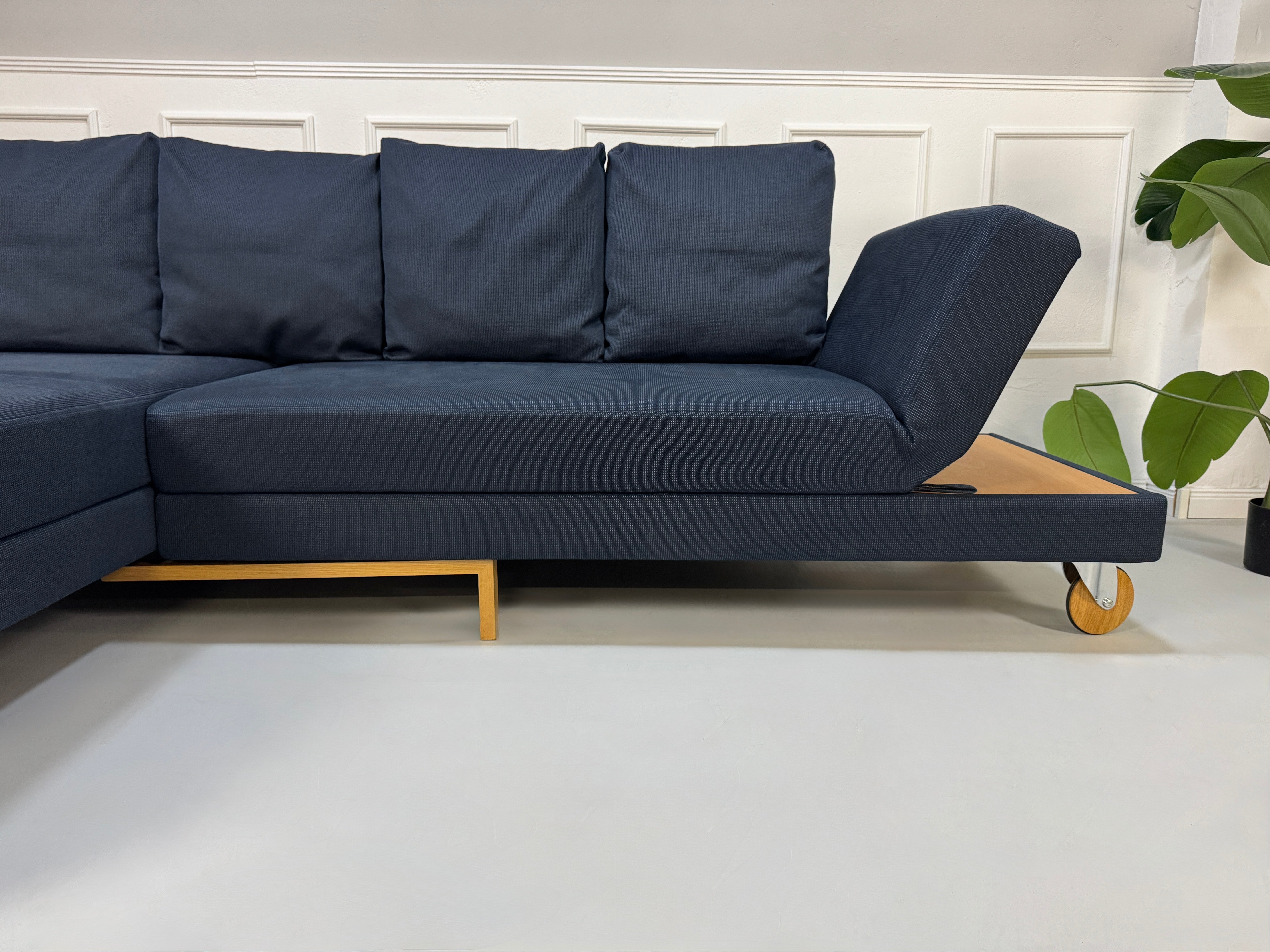 Gebrauchtes blaues Stoffsofa Brühl Modell Fourtwo vor einer modernen Wand.