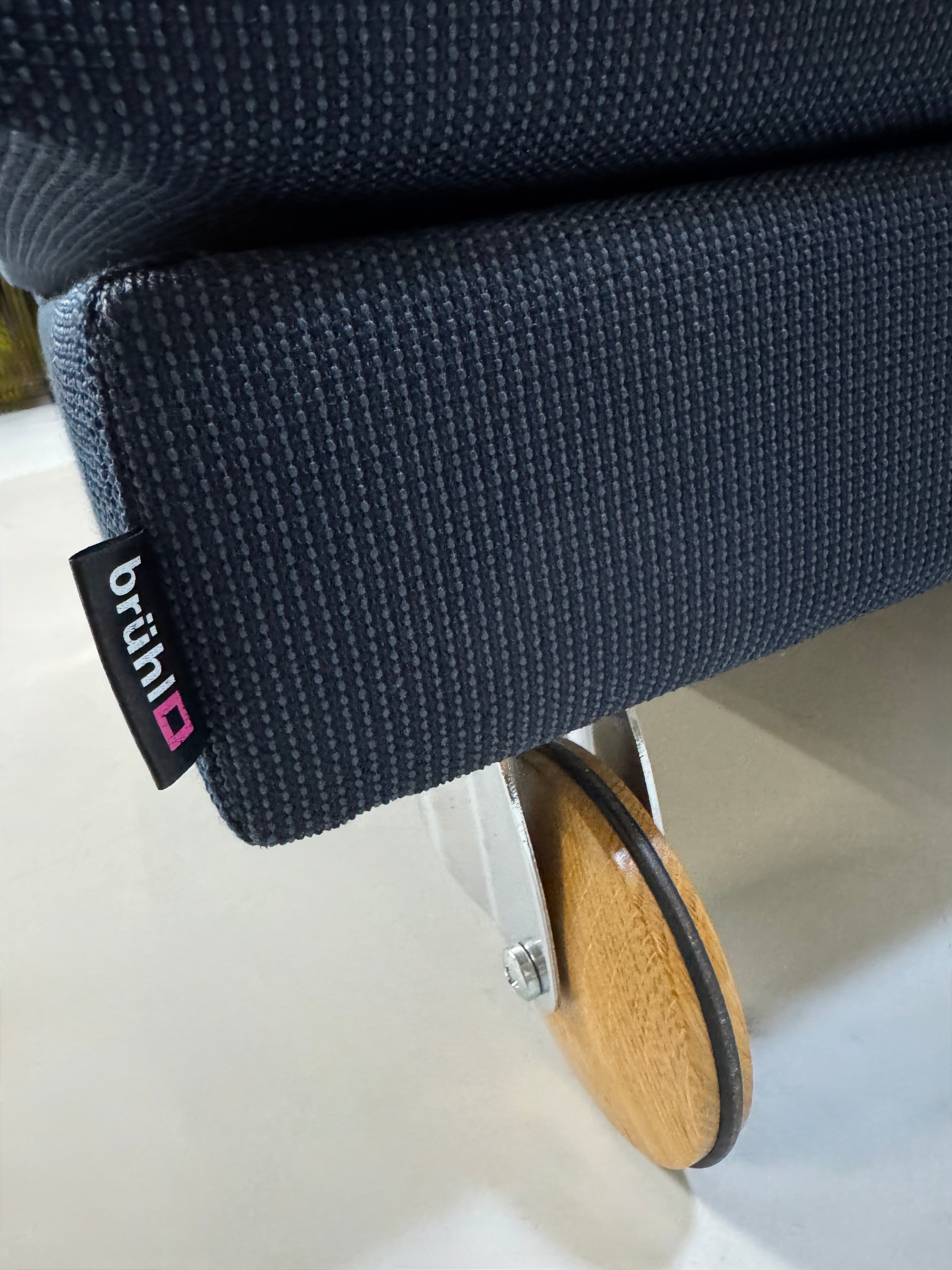 Gebrauchtes blaues Stoffsofa Brühl Modell Fourtwo vor einer modernen Wand.
