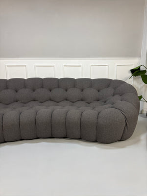 Gebrauchtes graues Stoffsofa Roche Bobois Modell Bubble vor einer modernen Wand.