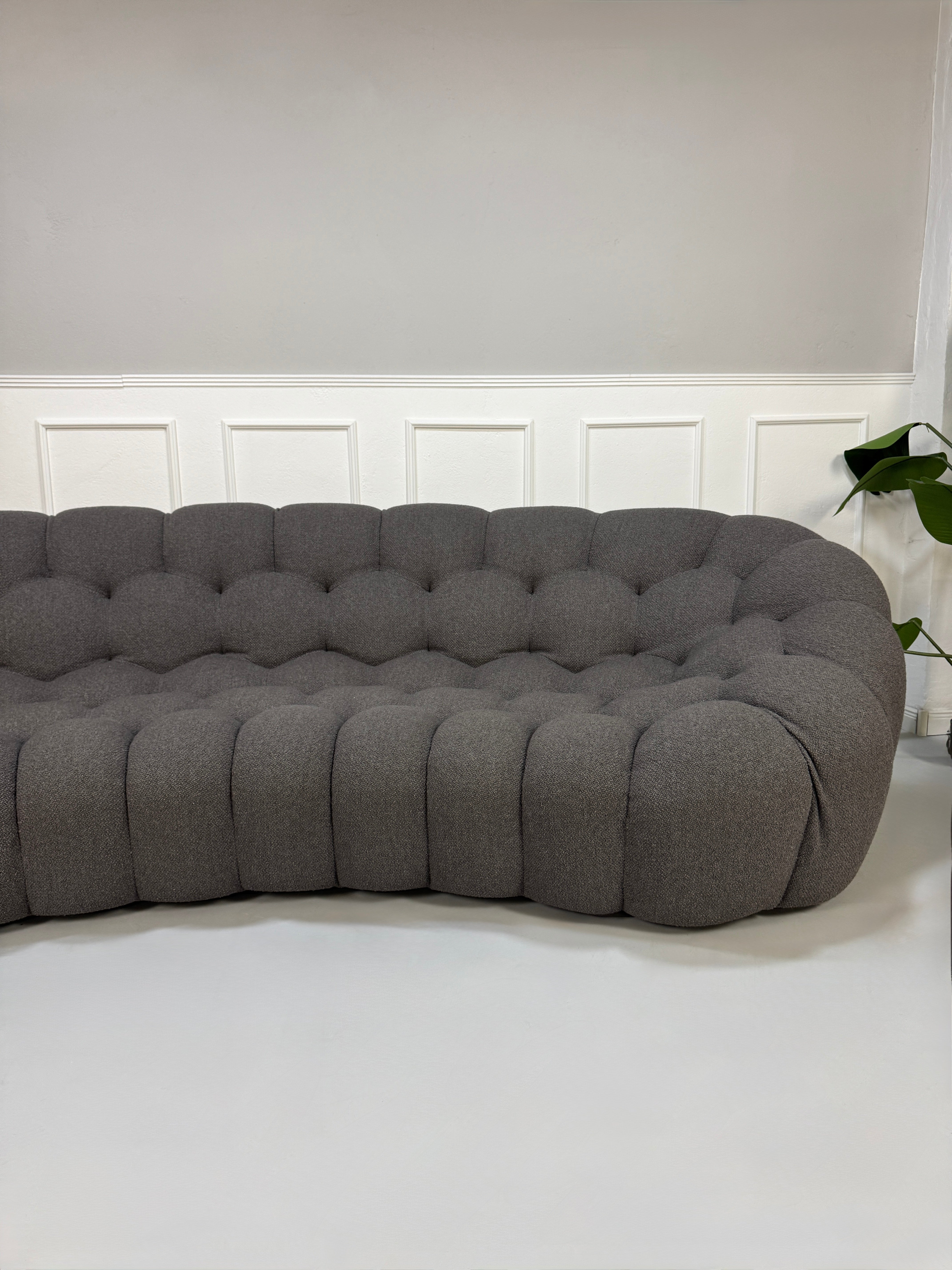 Gebrauchtes graues Stoffsofa Roche Bobois Modell Bubble vor einer modernen Wand.