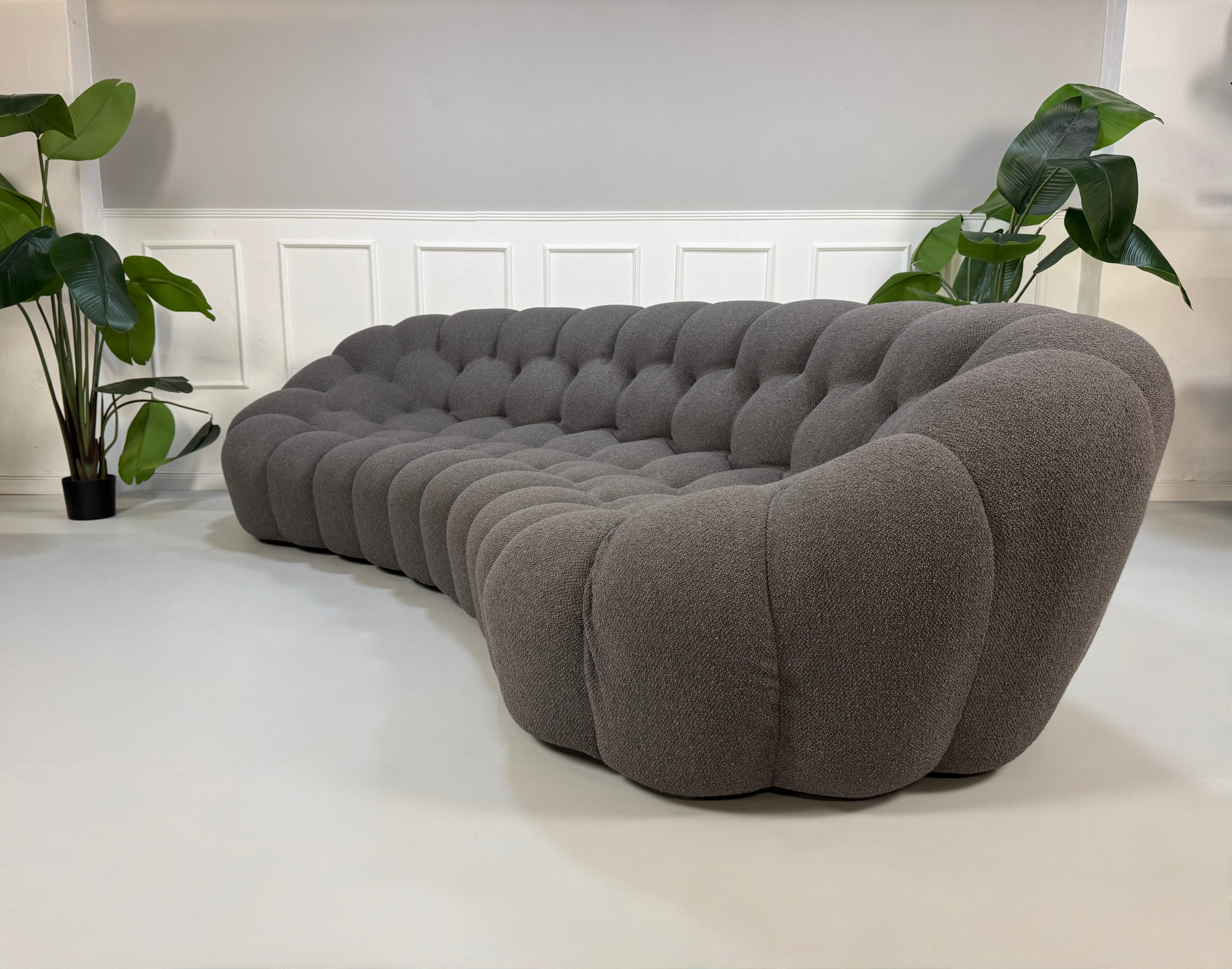Gebrauchtes graues Stoffsofa Roche Bobois Modell Bubble vor einer modernen Wand.
