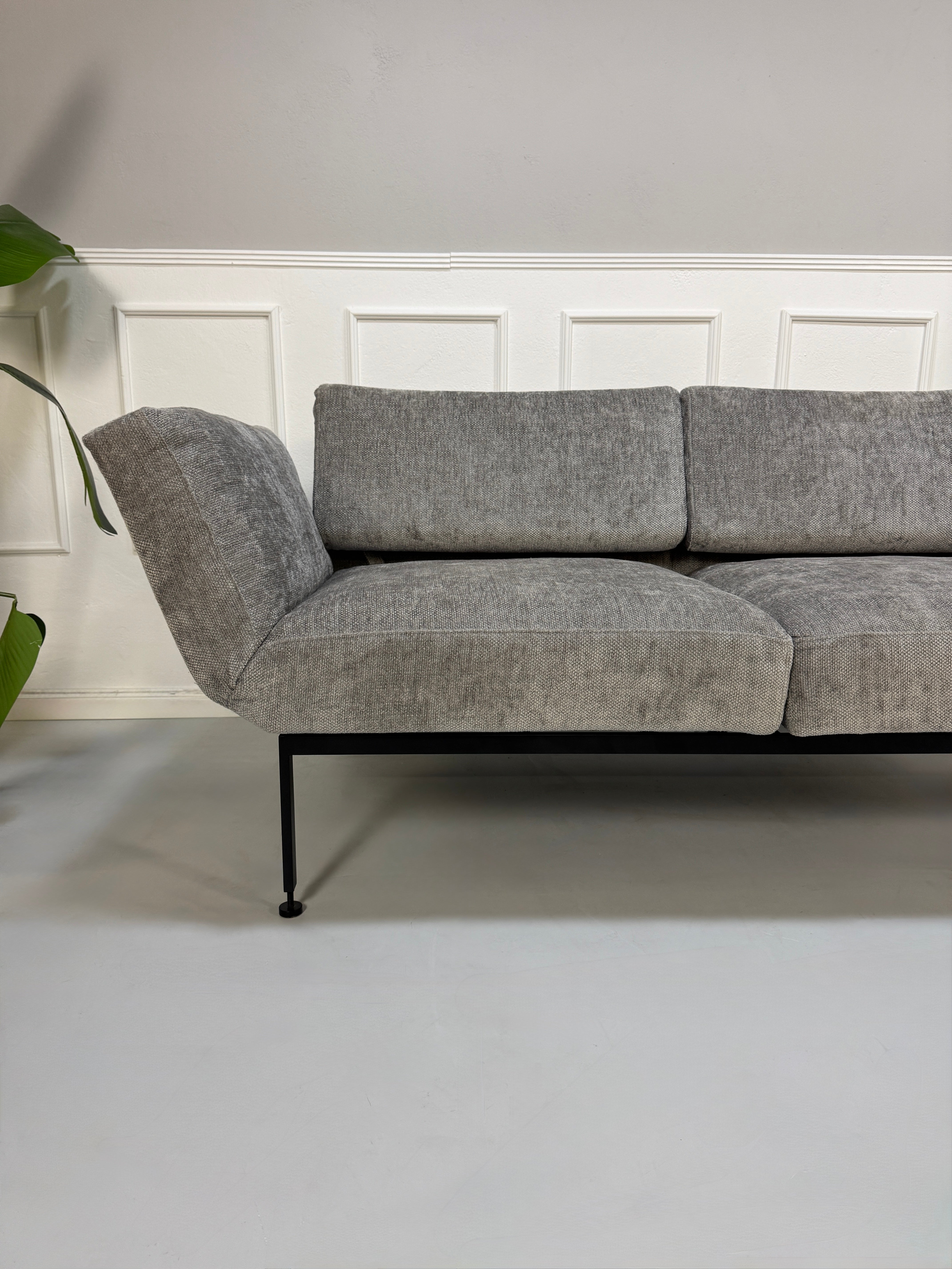Gebrauchtes graues Stoffsofa Brühl Modell Roro Spring vor einer modernen Wand.