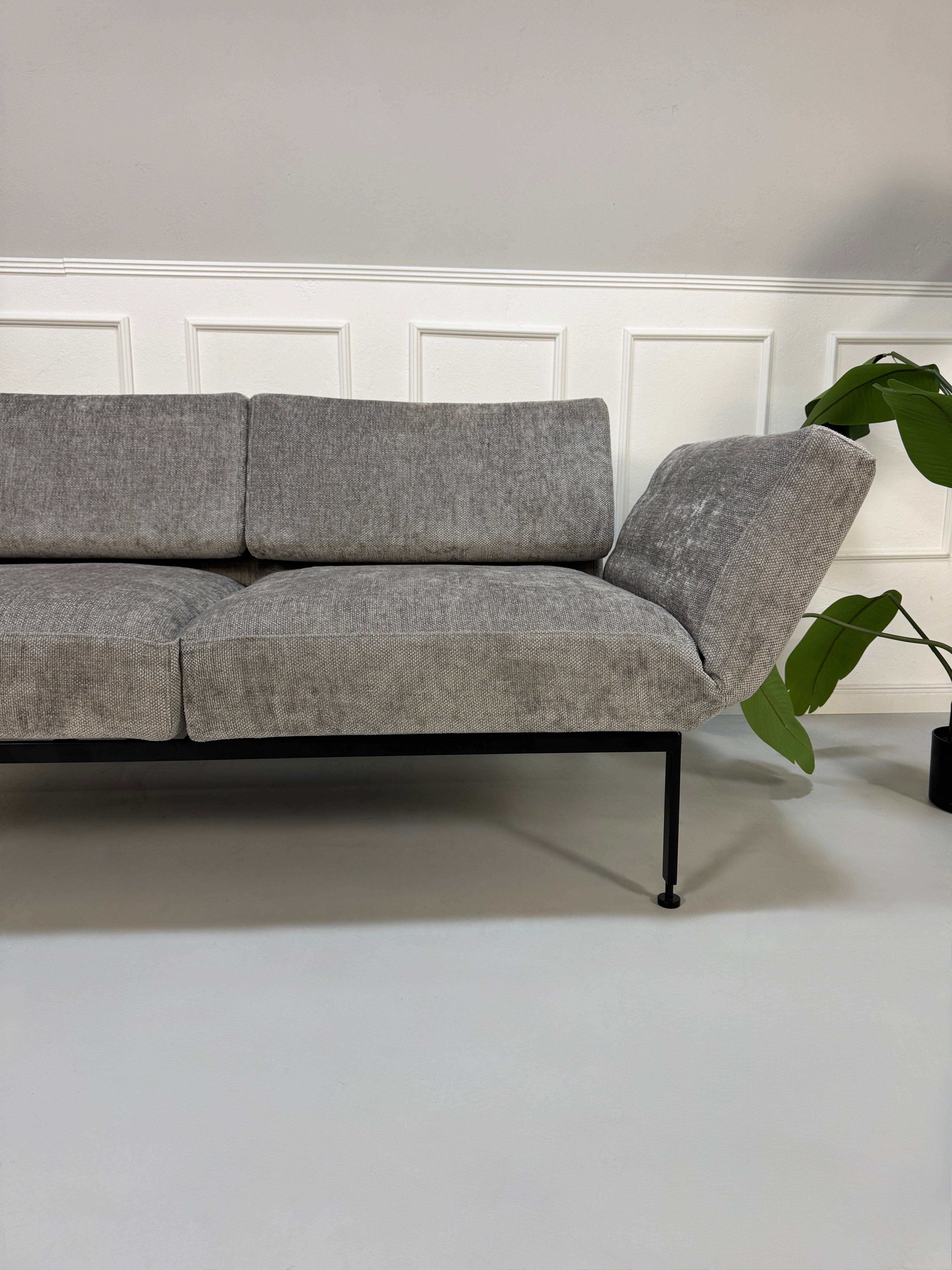 Gebrauchtes graues Stoffsofa Brühl Modell Roro Spring vor einer modernen Wand.