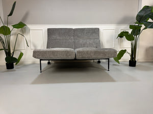 Gebrauchtes graues Stoffsofa Brühl Modell Roro Spring vor einer modernen Wand.