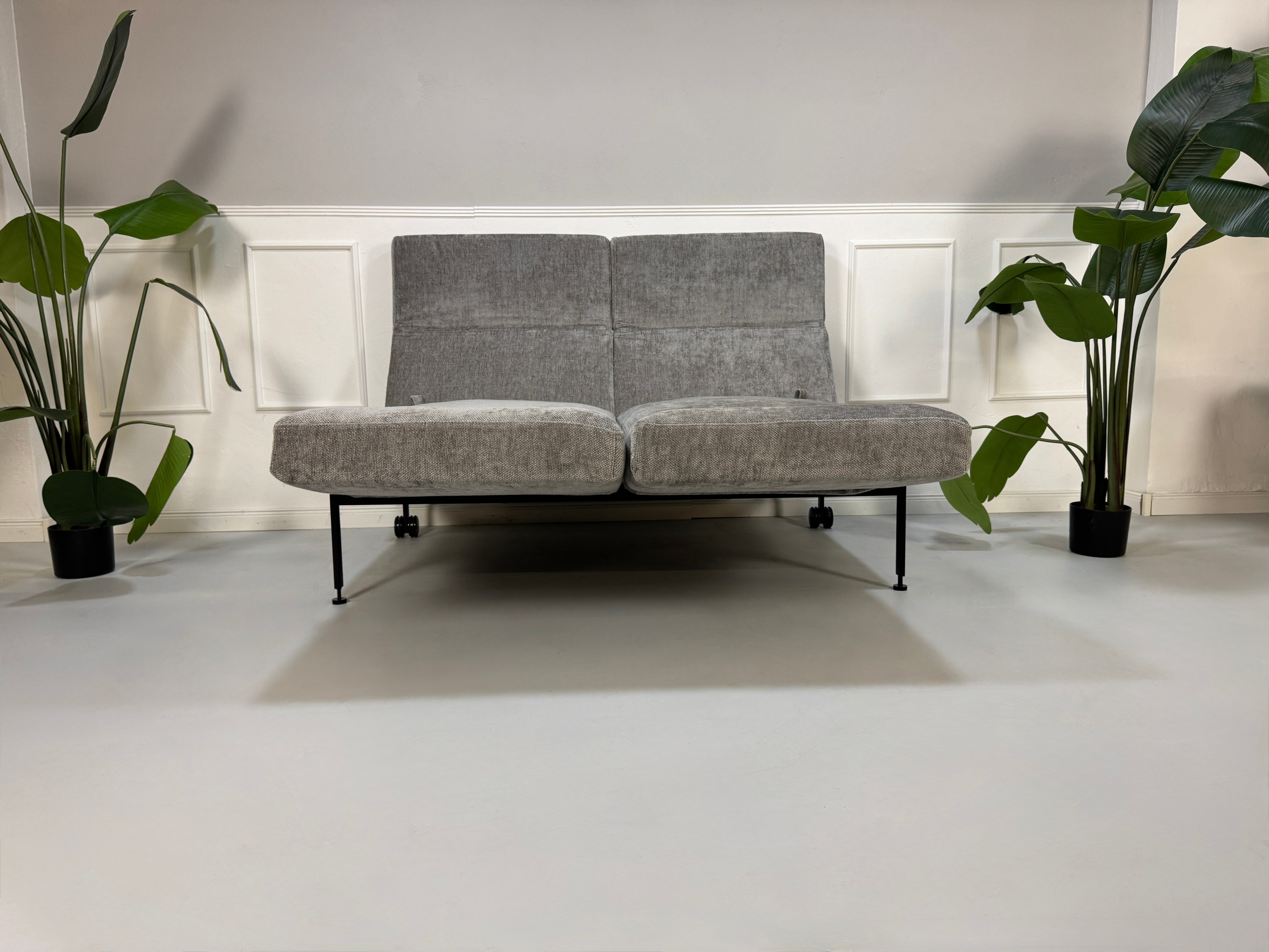 Gebrauchtes graues Stoffsofa Brühl Modell Roro Spring vor einer modernen Wand.