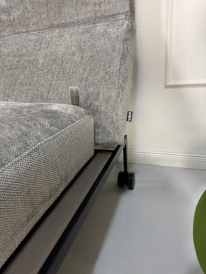Gebrauchtes graues Stoffsofa Brühl Modell Roro Spring vor einer modernen Wand.