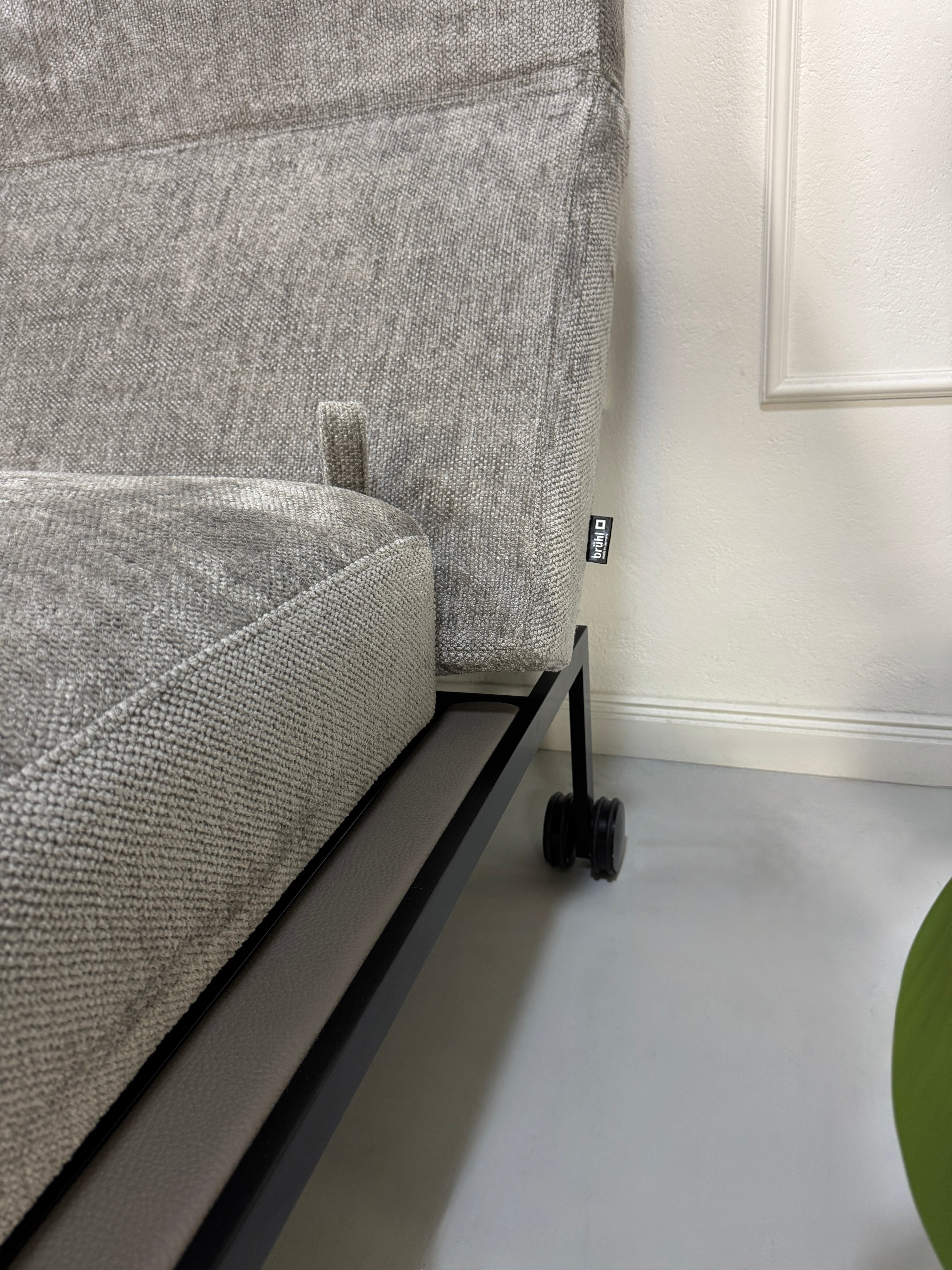 Gebrauchtes graues Stoffsofa Brühl Modell Roro Spring vor einer modernen Wand.