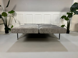 Gebrauchtes graues Stoffsofa Brühl Modell Roro Spring vor einer modernen Wand.