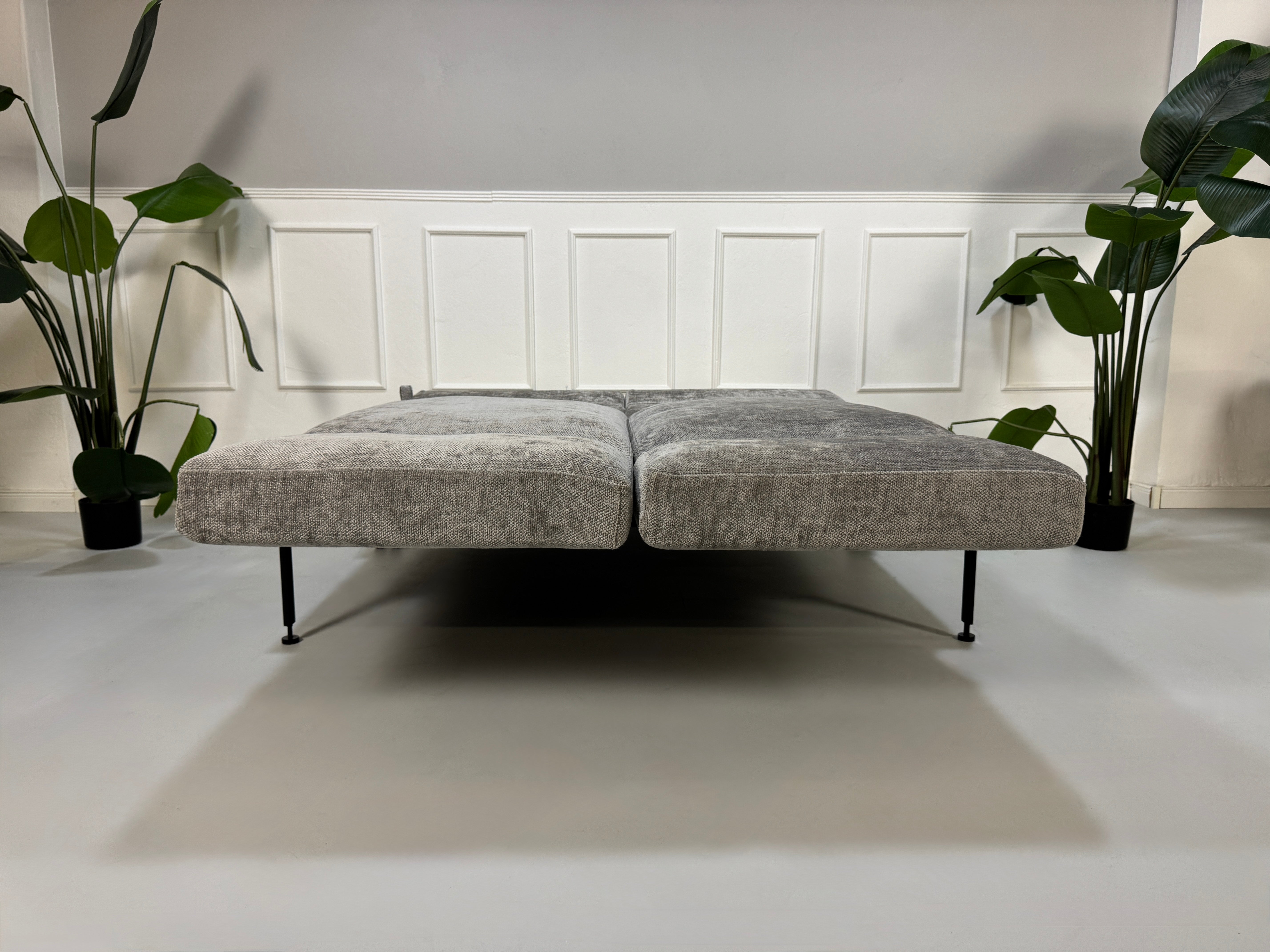 Gebrauchtes graues Stoffsofa Brühl Modell Roro Spring vor einer modernen Wand.