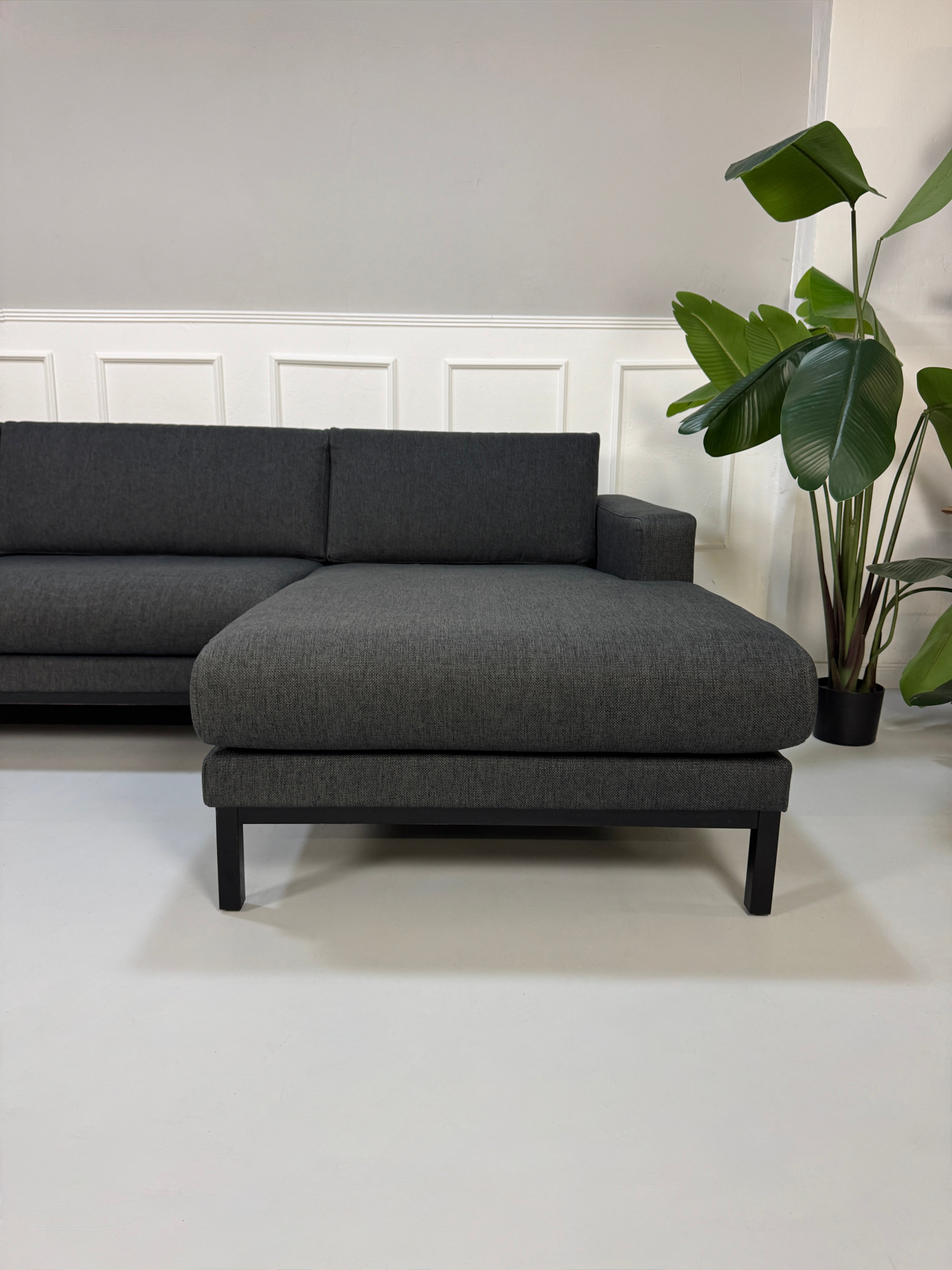 Gebrauchtes graues Stoffsofa Bolia Modell North vor einer modernen Wand.