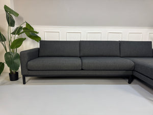 Gebrauchtes graues Stoffsofa Bolia Modell North vor einer modernen Wand.