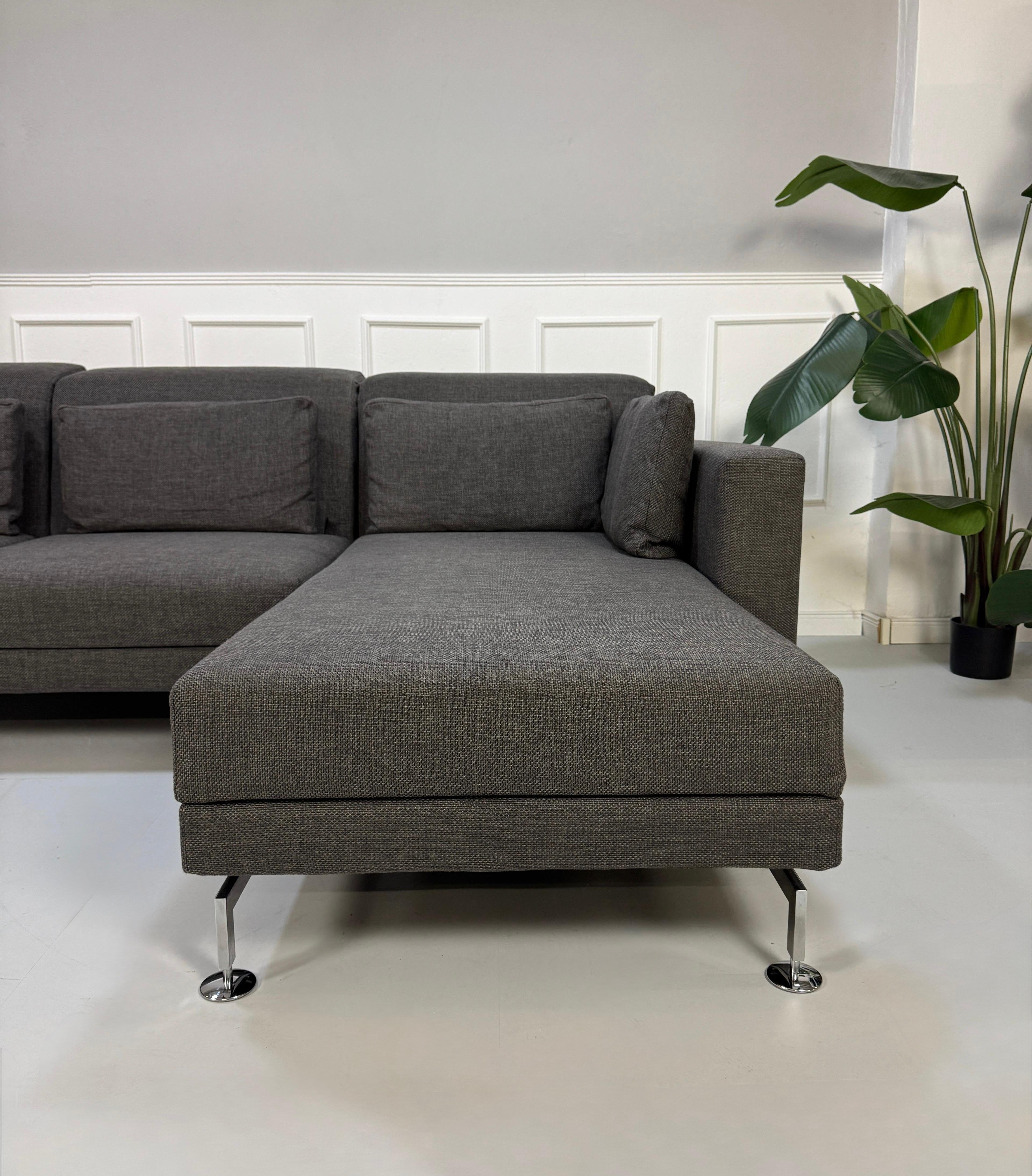 Gebrauchtes graues Stoffsofa Brühl Modell Moule vor einer modernen Wand.
