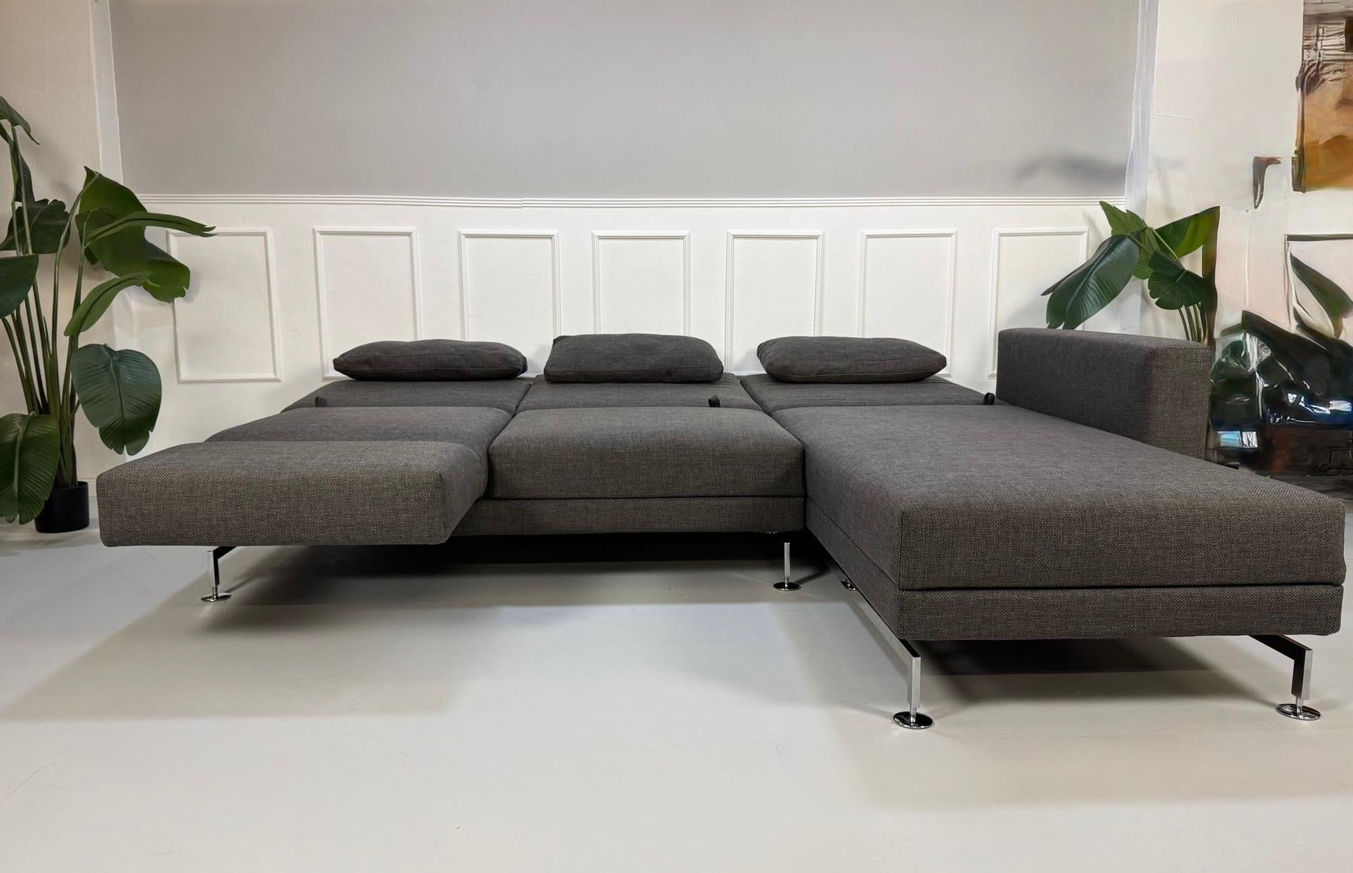 Gebrauchtes graues Stoffsofa Brühl Modell Moule vor einer modernen Wand.