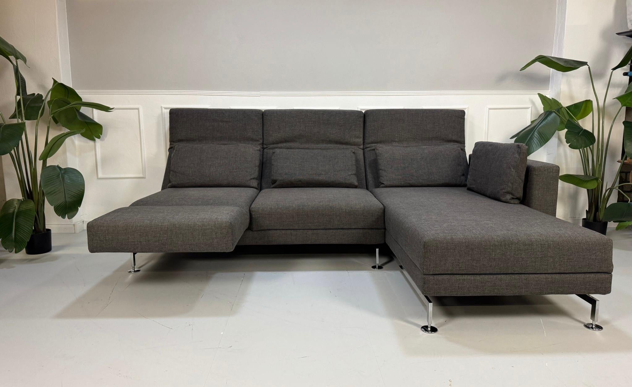 Gebrauchtes graues Stoffsofa Brühl Modell Moule vor einer modernen Wand.