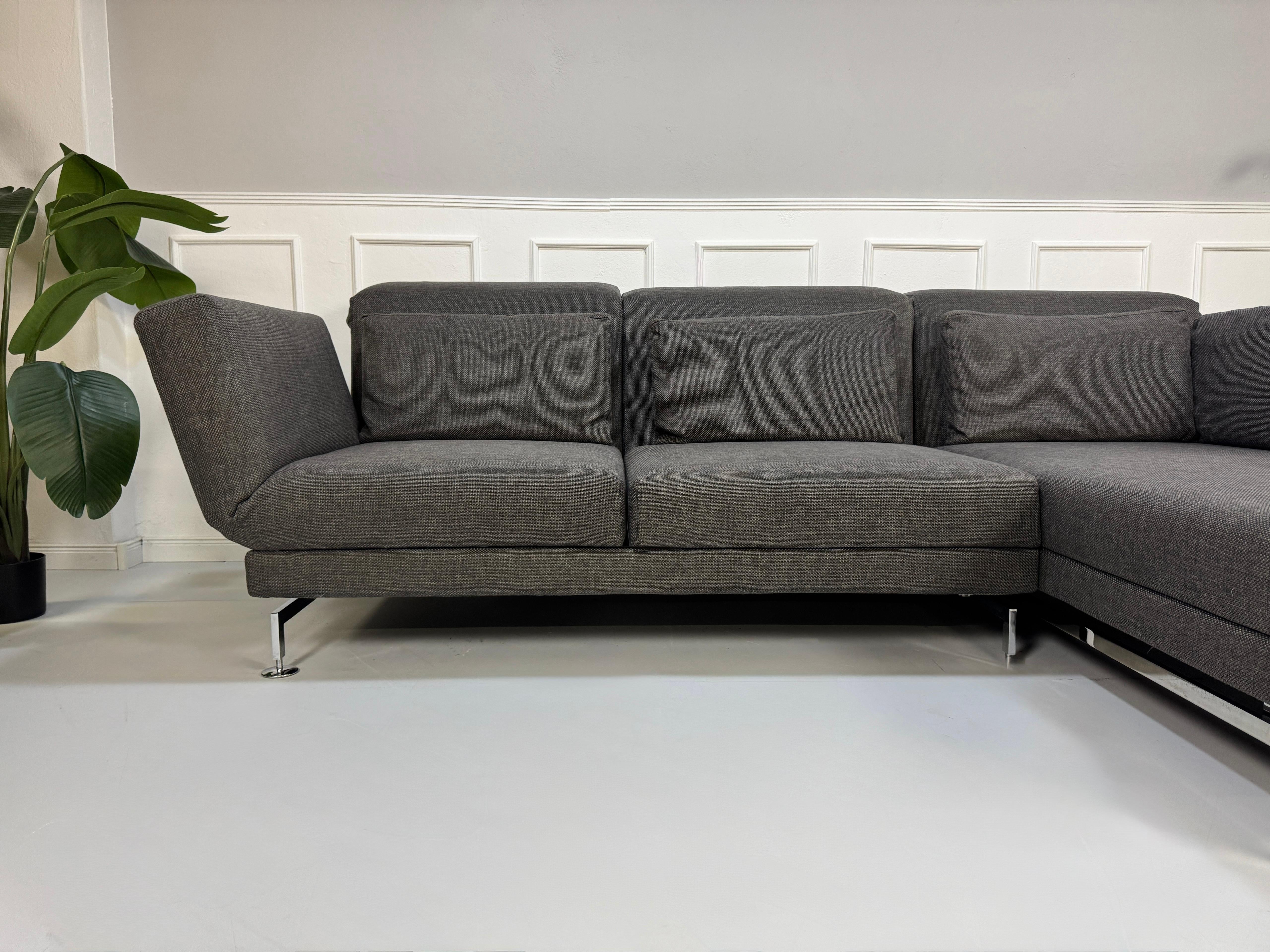 Gebrauchtes graues Stoffsofa Brühl Modell Moule vor einer modernen Wand.