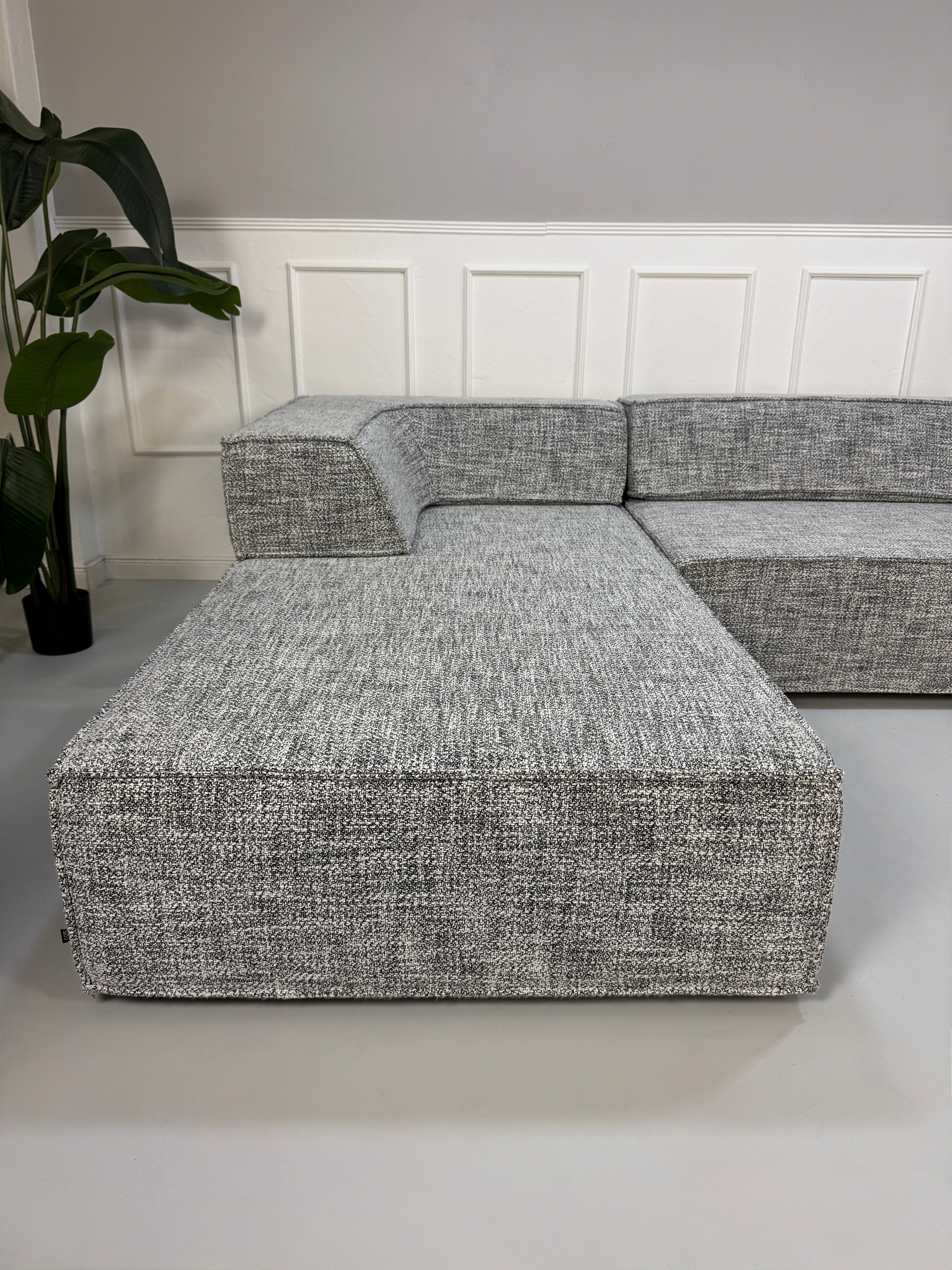 Gebrauchtes graues COR Trio Designer Stoff Sofa vor einer Wand, stilvoll und modern eingerichtet.