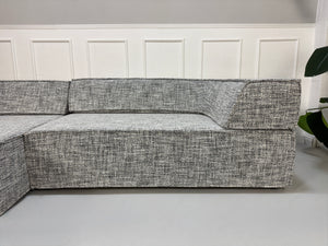 Gebrauchtes graues COR Trio Designer Stoff Sofa vor einer Wand, stilvoll und modern eingerichtet.